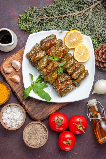 Vue de dessus délicieux dolma de feuilles avec des tranches de citron et des assaisonnements sur fond sombre plat de repas de viande dîner de feuilles