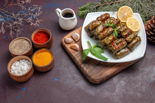 Photo gratuite vue de dessus de délicieux dolma de feuilles avec des tranches de citron et des assaisonnements sur le fond sombre plat de repas de viande feuille de dîner