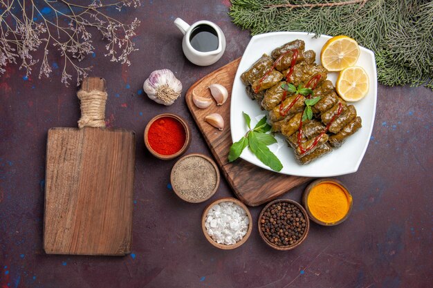 Vue de dessus délicieux dolma de feuilles avec des tranches de citron et des assaisonnements sur le fond sombre plat de viande feuille dîner repas nourriture