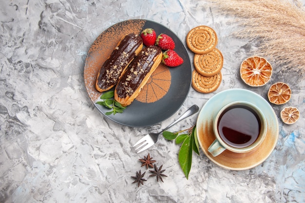 Vue de dessus de délicieux éclairs au chocolat avec du thé sur des biscuits de gâteau de dessert de table blanche