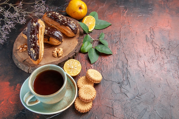 Vue de dessus de délicieux éclairs de choco avec une tasse de thé sur le gâteau sucré dessert table sombre