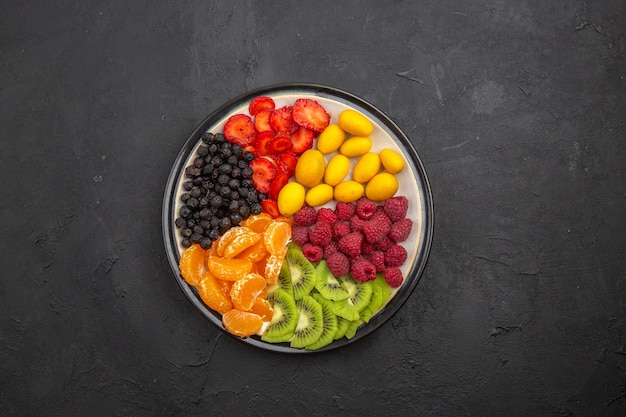 Vue de dessus de délicieux fruits tranchés à l'intérieur de la plaque sur une photo de régime mûr exotique de fruits tropicaux foncés