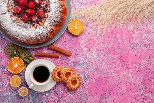 Vue de dessus délicieux gâteau aux fraises cuit au four avec des biscuits en poudre de sucre et du thé sur fond rose clair gâteau biscuit biscuit au sucre