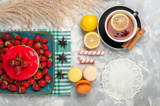 Vue de dessus délicieux gâteau aux fraises avec des fraises fraîches tasse de thé et macarons sur fond blanc