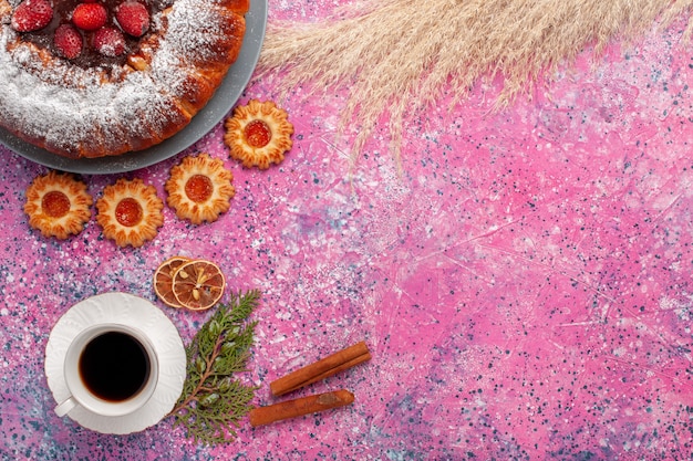 Vue de dessus délicieux gâteau aux fraises gâteau en poudre de sucre avec des biscuits à la cannelle et tasse de thé sur fond rose gâteau biscuits au sucre sucré tarte