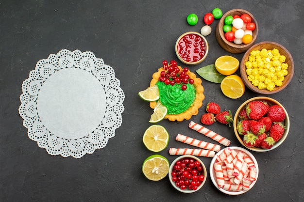 Vue de dessus délicieux gâteau avec des bonbons et des fruits sur un bureau sombre biscuit biscuit sucré