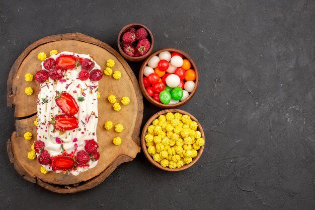 Vue de dessus délicieux gâteau crémeux avec fruits et bonbons sur fond sombre biscuit thé biscuit gâteau crème douce