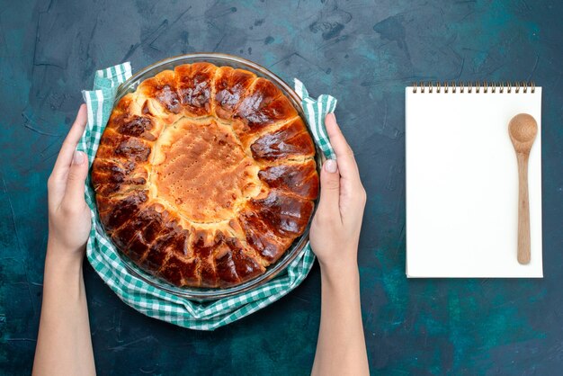 Vue de dessus un délicieux gâteau cuit au four rond formé à l'intérieur d'une casserole en verre sur le bureau bleu clair.