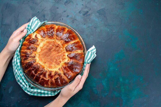 Vue de dessus délicieux gâteau cuit rond formé doux à l'intérieur de la casserole en verre sur le fond bleu clair.