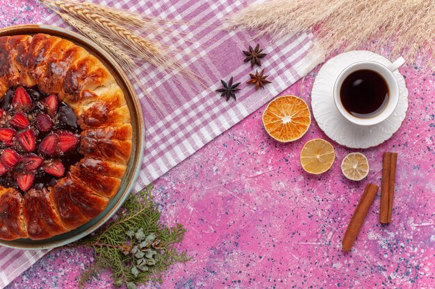 Vue de dessus délicieux gâteau fruité de tarte aux fraises avec une tasse de thé sur le rose