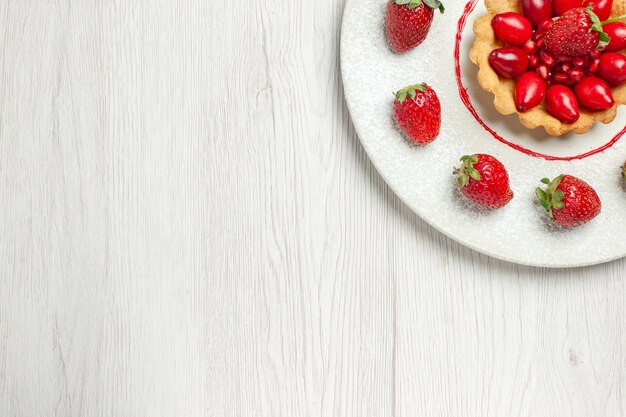 Vue de dessus délicieux gâteau avec des fruits frais à l'intérieur de la plaque sur le bureau blanc