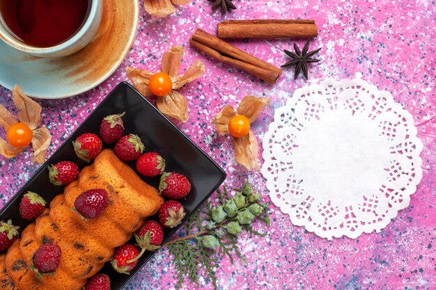 Vue de dessus délicieux gâteau à l'intérieur du moule à gâteau noir avec des fraises rouges fraîches et du thé sur le bureau rose.