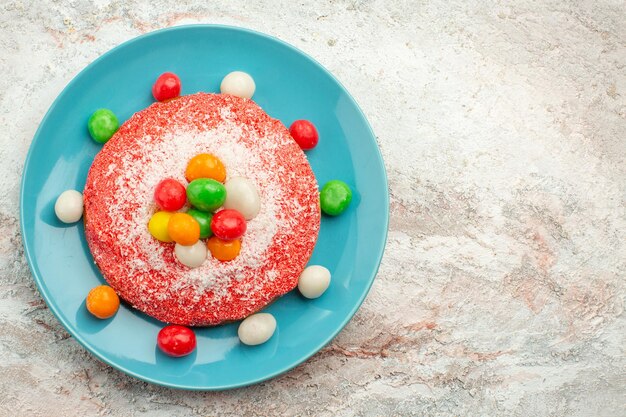 Vue de dessus un délicieux gâteau rose avec des bonbons colorés à l'intérieur de la plaque sur un dessert de gâteau à tarte aux couleurs de bonbons arc-en-ciel de surface blanche