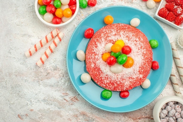 Vue de dessus délicieux gâteau rose avec des bonbons colorés sur un sol blanc bonbons dessert couleur arc-en-ciel goodie cake