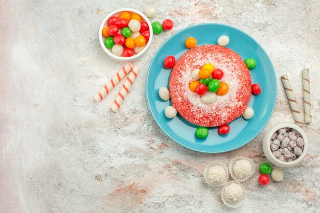 Vue de dessus délicieux gâteau rose avec des bonbons colorés sur une surface blanche bonbons dessert couleur arc-en-ciel goodie cake