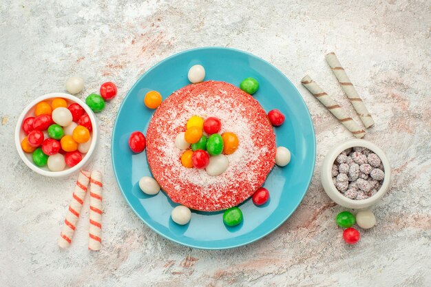 Vue de dessus délicieux gâteau rose avec des bonbons colorés sur une surface blanche bonbons dessert couleur arc-en-ciel goodies cake