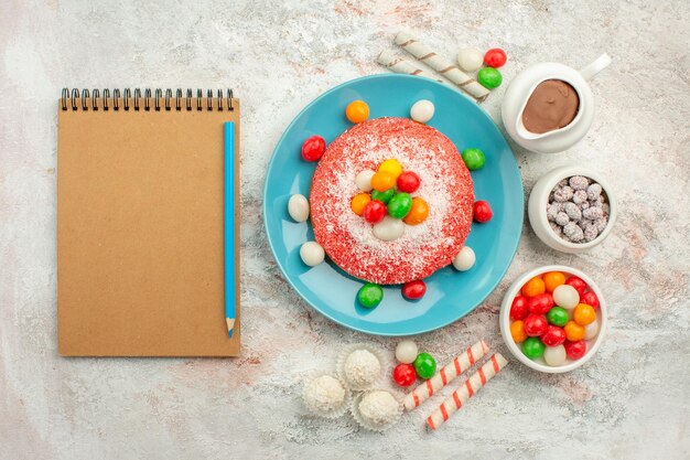 Vue de dessus délicieux gâteau rose avec des bonbons colorés sur une surface blanche dessert couleur goodie arc-en-ciel gâteau bonbons