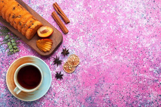 Vue de dessus délicieux gâteau sucré et délicieux avec une tasse de thé et de cannelle sur le bureau rose.