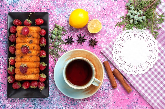 Vue de dessus délicieux gâteau avec thé au citron fraises fraîches rouges sur le bureau rose.