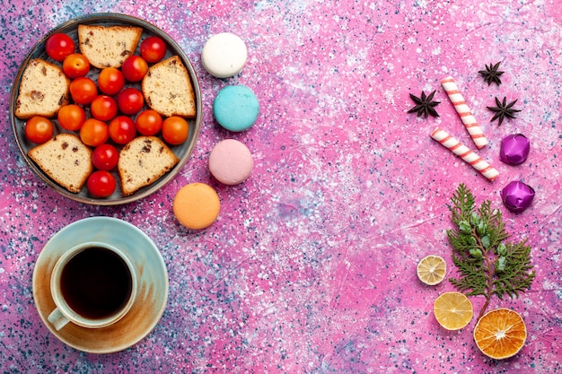 Vue de dessus délicieux gâteau en tranches avec macarons de prunes fraîches aigres et tasse de thé sur la surface rose