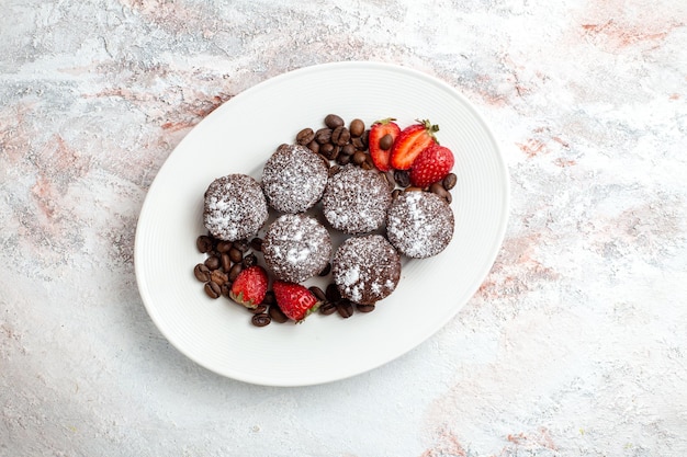 Vue de dessus de délicieux gâteaux au chocolat avec des fraises et des pépites de chocolat sur une surface blanche