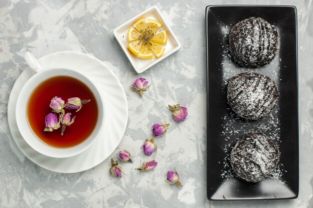 Vue de dessus de délicieux gâteaux au chocolat avec glaçage avec une tasse de thé sur le gâteau de bureau blanc clair biscuit sucre biscuit chocolat cacao