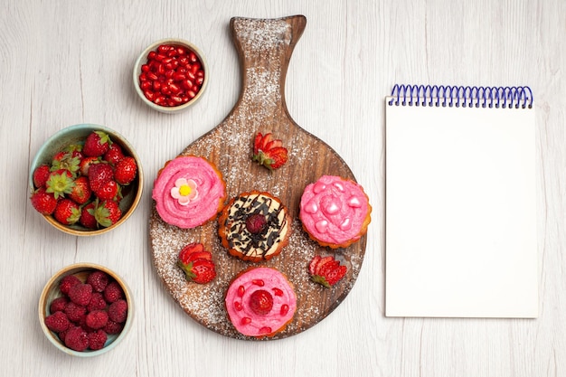 Vue de dessus de délicieux gâteaux aux fruits desserts crémeux avec des baies et des fruits sur fond blanc thé à la crème gâteau de dessert aux biscuits sucrés