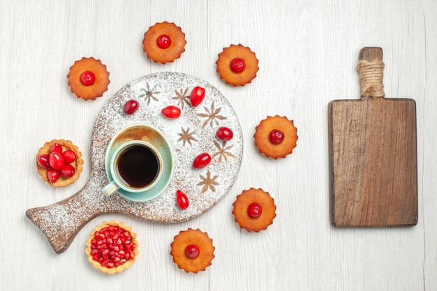 Vue de dessus de délicieux gâteaux aux fruits et tasse de thé sur un bureau blanc