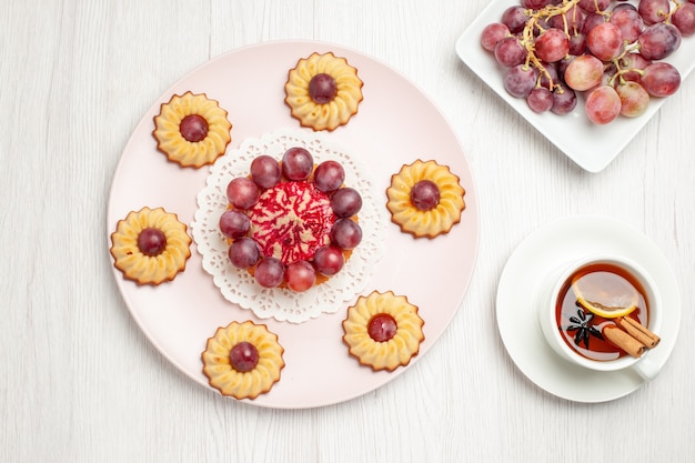 Vue de dessus de délicieux gâteaux aux raisins avec une tasse de thé sur la table blanche biscuit tarte biscuit biscuit