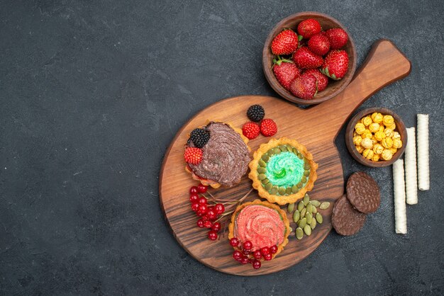 Vue de dessus de délicieux gâteaux crémeux aux fruits sur la table noire biscuit sucré