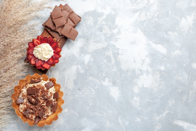 Vue de dessus de délicieux gâteaux crémeux avec des barres de chocolat sur le bureau blanc gâteau biscuit sucre sucré cuire