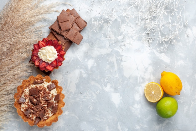 Vue de dessus de délicieux gâteaux crémeux avec des barres de chocolat et des citrons frais sur le gâteau de bureau blanc biscuit sucré cuire au four