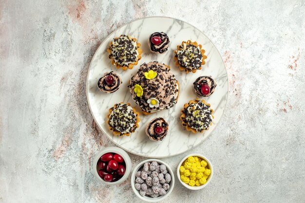 Vue de dessus de délicieux gâteaux crémeux avec des bonbons sur une surface blanche claire gâteau au thé biscuit crème d'anniversaire douce