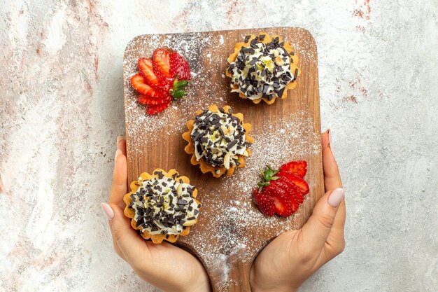 Vue de dessus de délicieux gâteaux crémeux avec des fraises tranchées sur une surface blanche crème sucre gâteau au thé biscuit anniversaire sucré