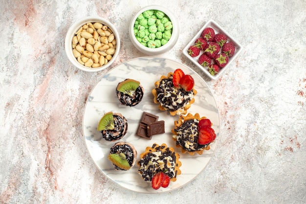 Vue de dessus de délicieux gâteaux crémeux avec des noix et des bonbons sur une surface blanche biscuit gâteau aux fruits tarte à la crème biscuit au thé