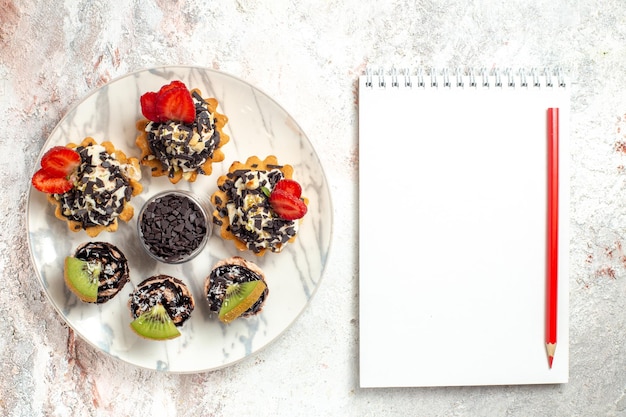 Vue de dessus de délicieux gâteaux crémeux petits desserts pour le thé avec des pépites de chocolat sur une surface blanche gâteau aux fruits crème biscuit tarte thé