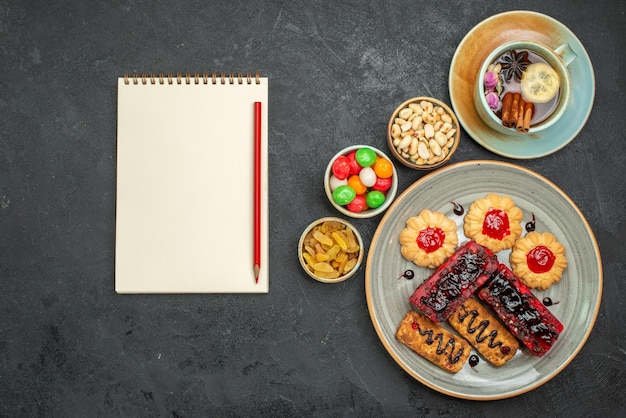 Vue de dessus de délicieux gâteaux fruités avec des biscuits et une tasse de thé dans l'obscurité