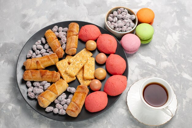 Vue de dessus de délicieux gâteaux avec des macarons de bagels et une tasse de thé sur une surface blanche grise