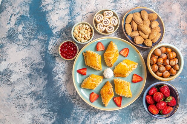 Vue de dessus de délicieux gâteaux sucrés avec des fruits et des noix sur un bureau bleu