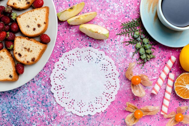 Vue de dessus de délicieux gâteaux en tranches avec une tasse de café et des fraises rouges sur le bureau rose clair