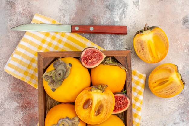 Vue de dessus de délicieux kakis et figues coupées dans une boîte en bois sur fond nude