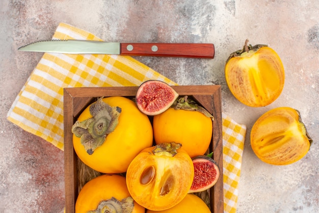 Vue de dessus de délicieux kakis et figues coupées dans une boîte en bois sur fond nude