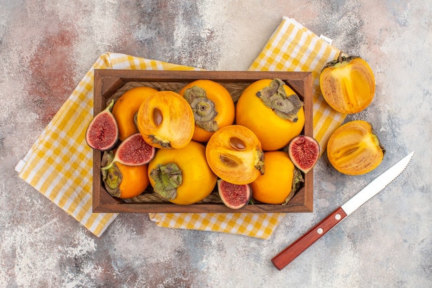 Photo gratuite vue de dessus de délicieux kakis et figues coupées dans une boîte en bois un kaki coupé un couteau sur fond nu