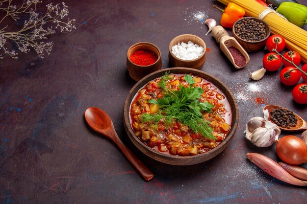 Vue de dessus de délicieux légumes cuits tranchés avec des légumes verts et des assaisonnements sur une soupe de table sombre