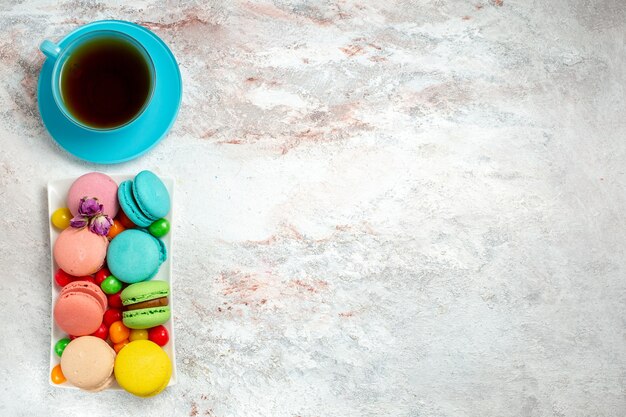 Vue de dessus de délicieux macarons colorés petits gâteaux avec des bonbons sur un bureau blanc