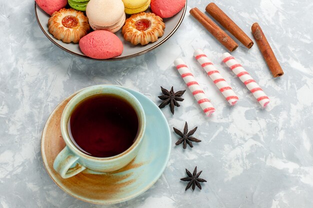 Vue de dessus de délicieux macarons français avec des biscuits à la cannelle et du thé sur un bureau blanc léger cuire au four gâteau biscuit sucre sweet photo