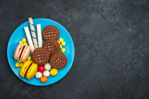 Vue de dessus de délicieux macarons français avec des bonbons et des biscuits au chocolat sur fond gris foncé biscuit gâteau au sucre biscuit sucré