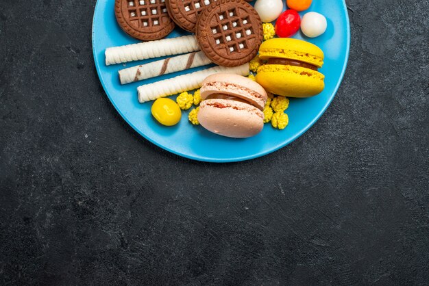 Vue de dessus de délicieux macarons français avec des bonbons et des biscuits au chocolat sur fond gris foncé biscuit gâteau au sucre sweet bake cookies