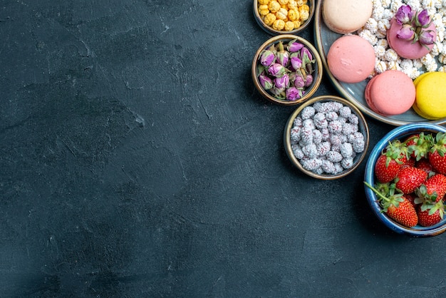 Vue de dessus de délicieux macarons français avec des bonbons et des fruits sur un sol gris