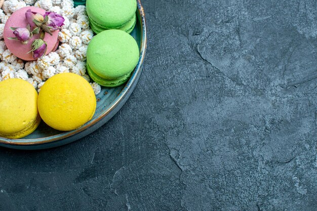 Vue de dessus de délicieux macarons français avec des bonbons à l'intérieur du plateau sur un espace sombre